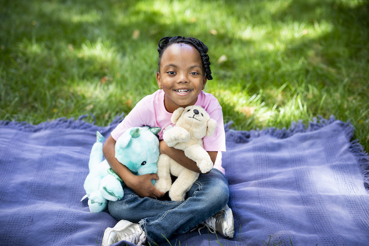 Small girl holding plush toys will sitting on a blanket